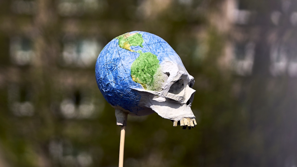 A sign with a skull and crossbones designed as a globe is held by participants in a climate demonstration on April 18, 2026.