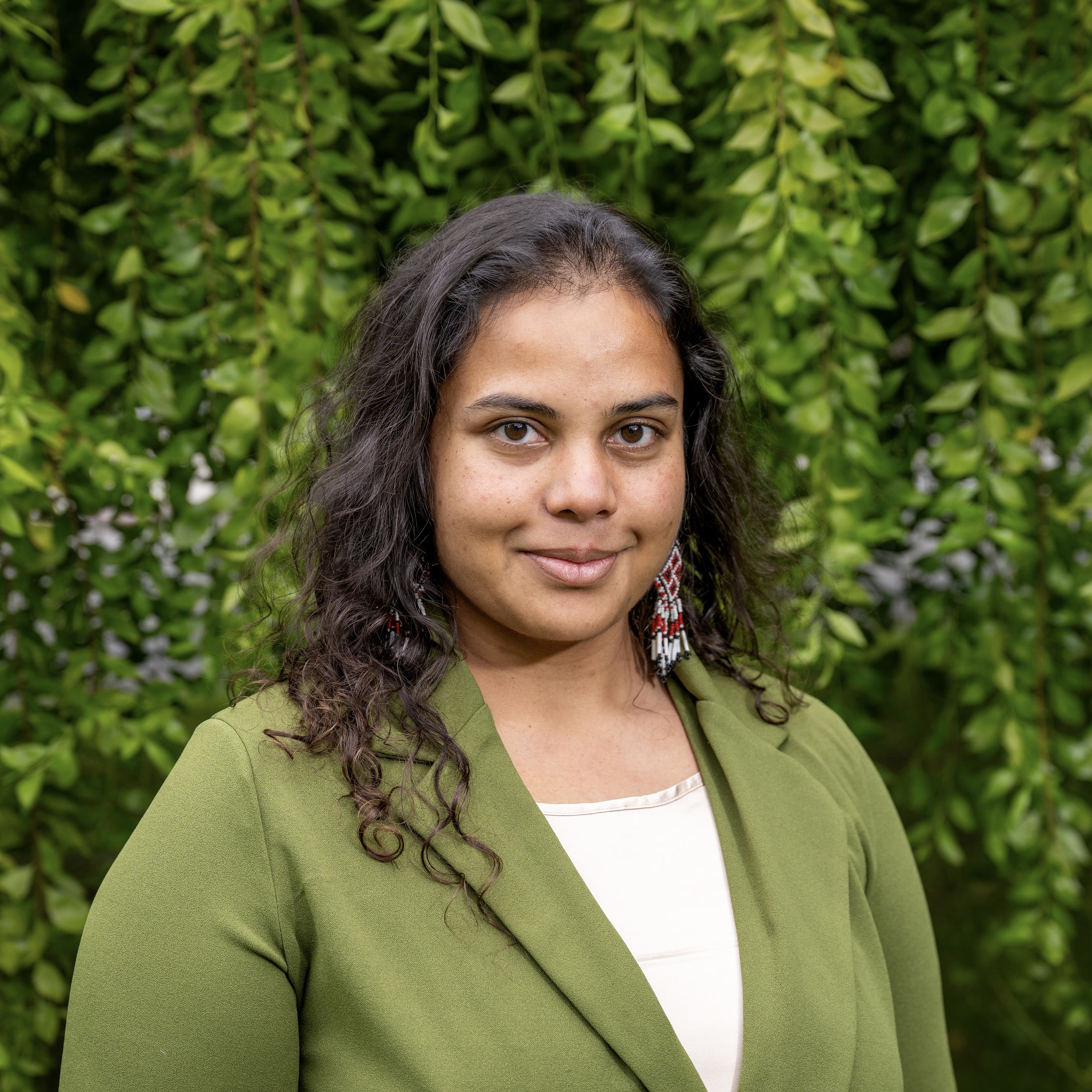 Manisha smiles at the camera in a white blouse and green suit jacket.