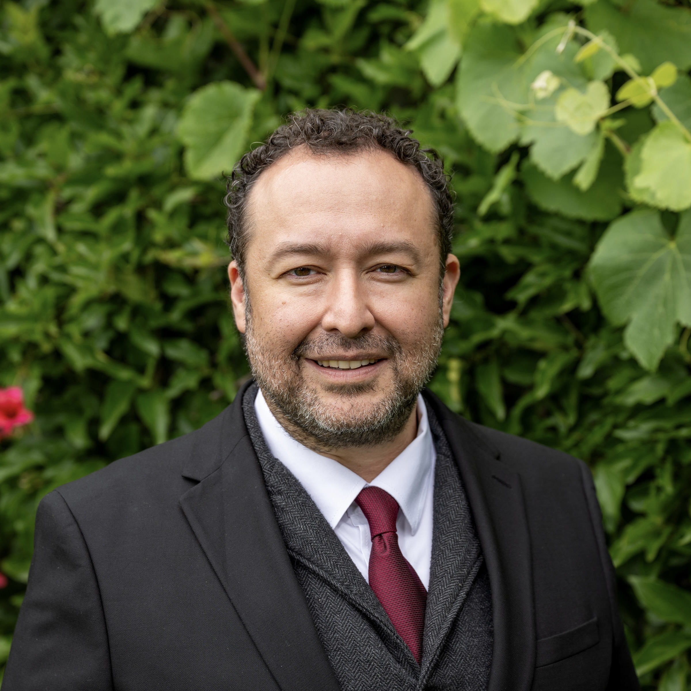 Christian smiles at the camera in a black suit jacket, white collared shirt, and red tie.