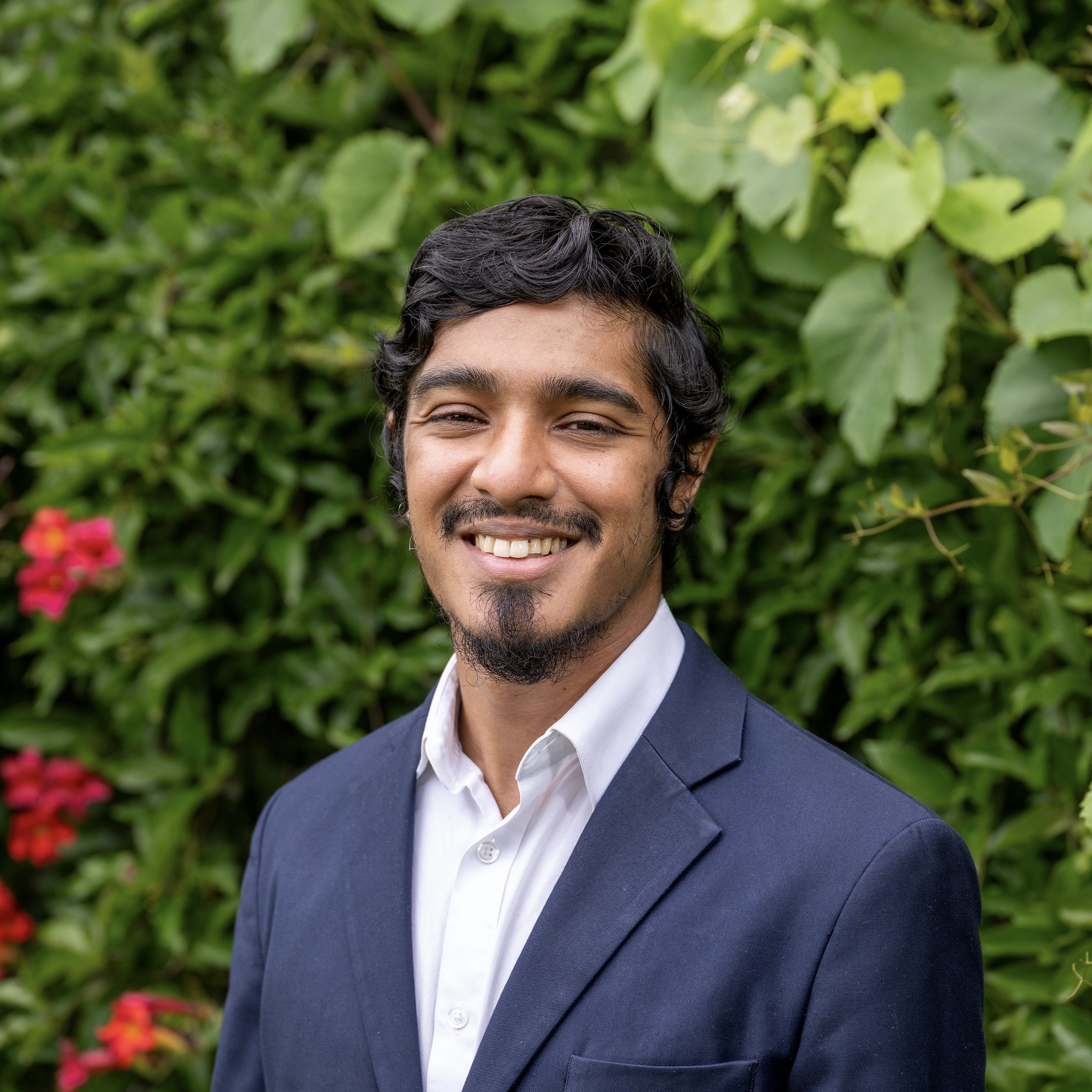 Mohammad smiles at the camera in a white button-up shirt and a dark blue suit jacket.