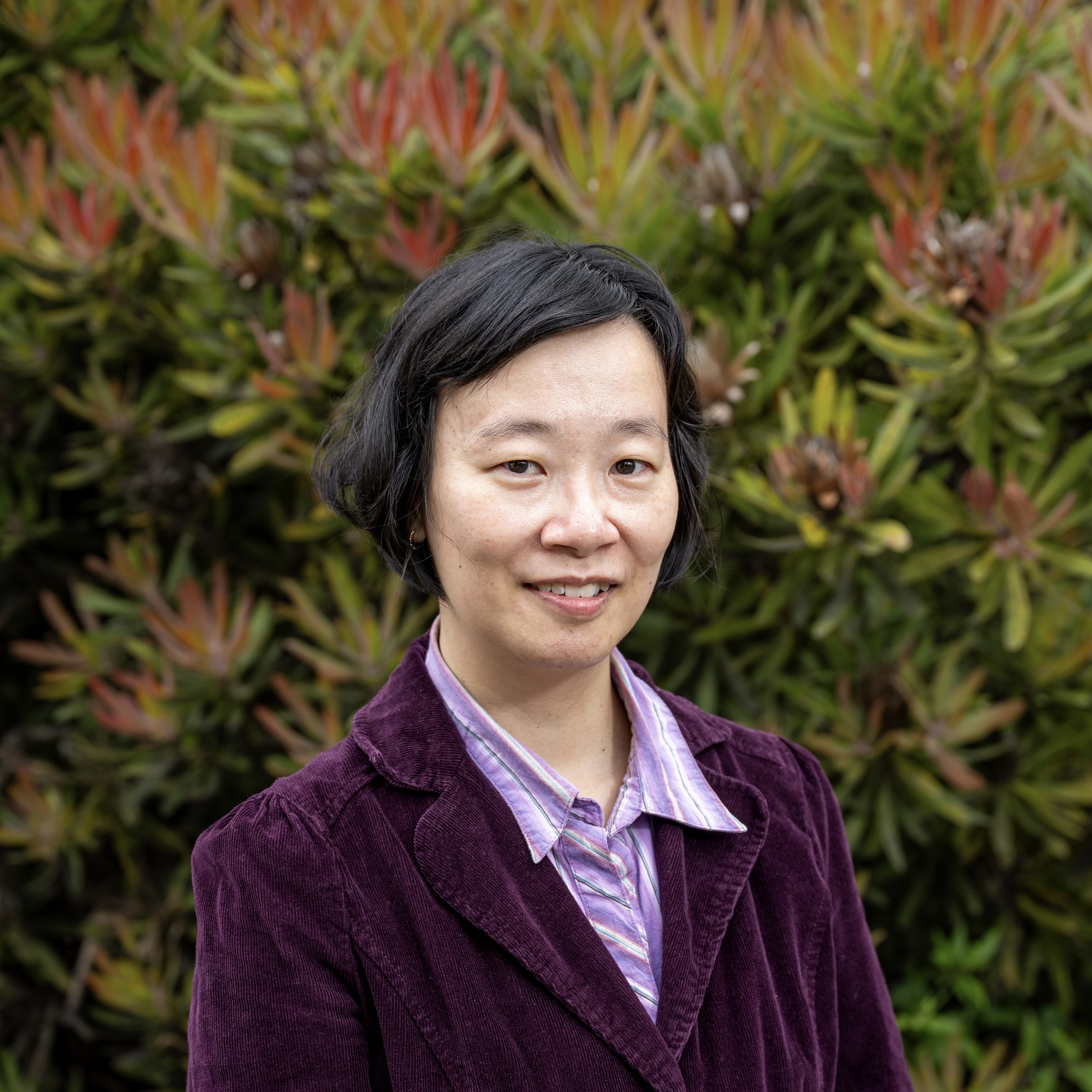 Amy smiles at the camera in a striped, purple blouse and dark purple suit jacket.