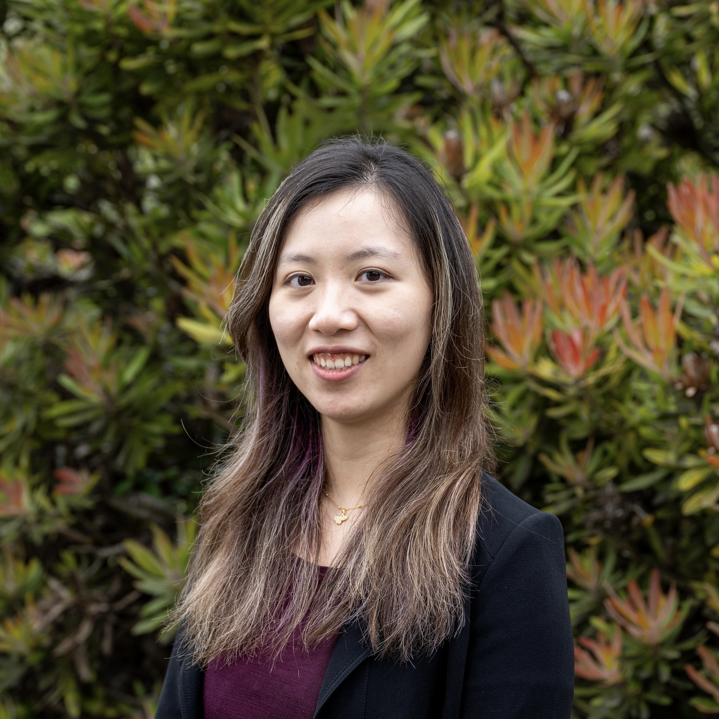 Jenny smiles at the camera in a maroon top and black suit jacket.