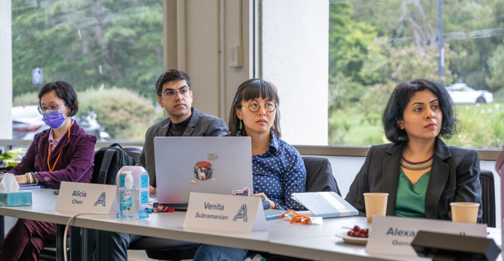 4 Fellows sit alongside a long table during a fellowship teaching session. They are taking notes on their computers and turned to face the front of the room.