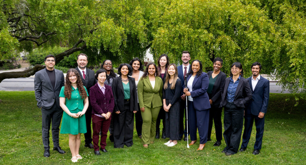 The 2026 Aspen Fellows stand shoulder to shoulder smiling against a green, tree backdrop.