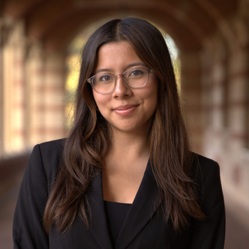 Danielle poses for the camera beneath brick building arches in a black blazer and black blouse.