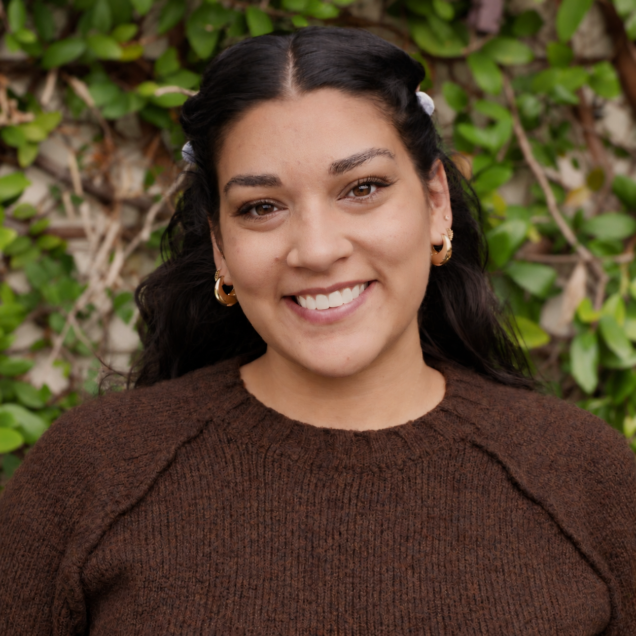 Kateri smiles at the camera in a brown sweater against a backdrop of green ivory.