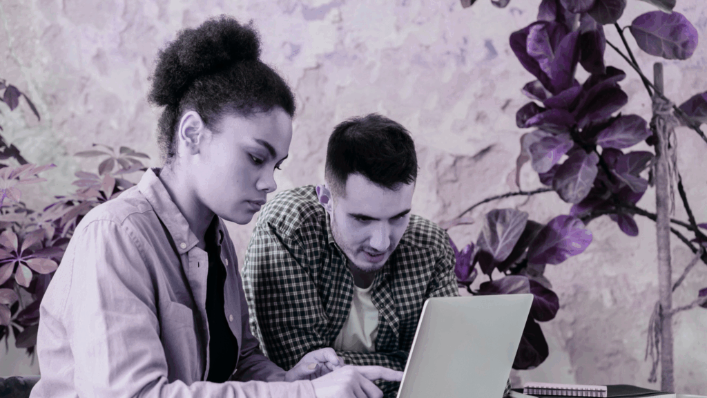 Two people sitting at a desk, leaning over a laptop.